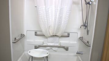 A bathroom with a shower, grab bars, a small sink, and a toilet.