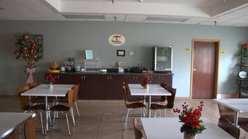 A dining area with tables and chairs, a counter with a coffee machine, and a clock on the wall.