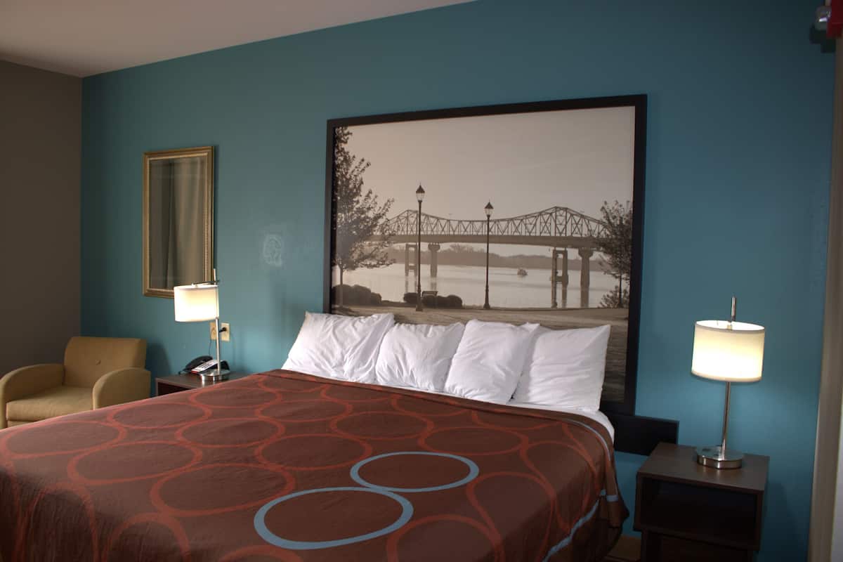 A hotel room with a large bed, two bedside lamps, a chair, and a framed picture on the wall.