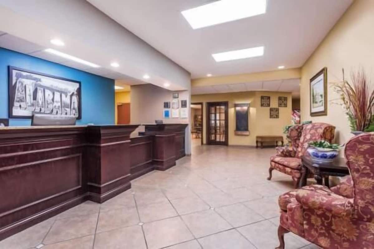 A reception area with a wooden reception desk, a blue wall with a framed picture, and a seating area with patterned chairs.