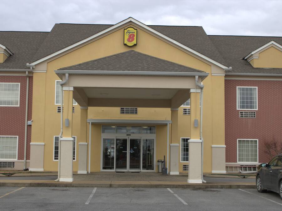 A hotel entrance with a yellow facade, a brick building on one side, and a car parked in the driveway.