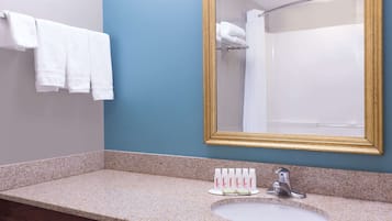 A bathroom with a granite countertop, a white sink, a gold-framed mirror, and a towel rack with white towels.
