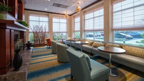 A hotel lobby with a seating area, large windows, and a fireplace. - Hilton Garden Inn Tupelo (Tupelo)