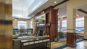 A spacious lobby with a fireplace, comfortable seating, and large windows offering views of the outside. - Hilton Garden Inn Tupelo (Tupelo)