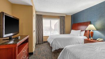 A hotel room with two beds, a TV, a desk, and a window with curtains.