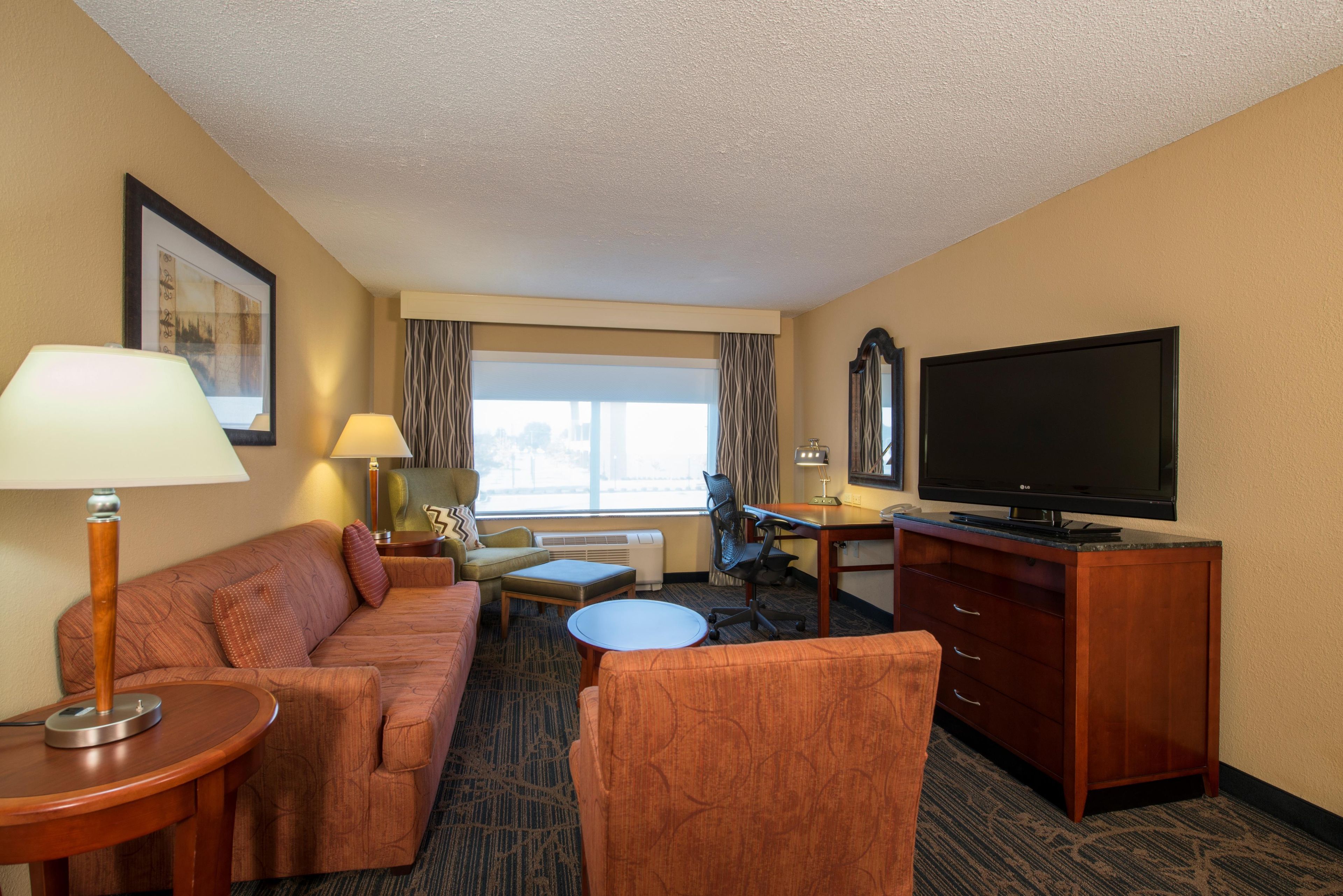 A hotel room with a sofa, a desk, a television, and a window with curtains.