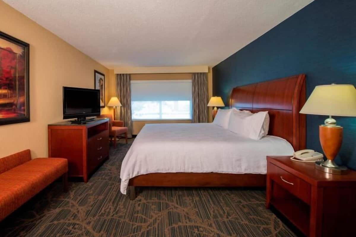 A hotel room with a bed, a television, a desk, a chair, and a window.