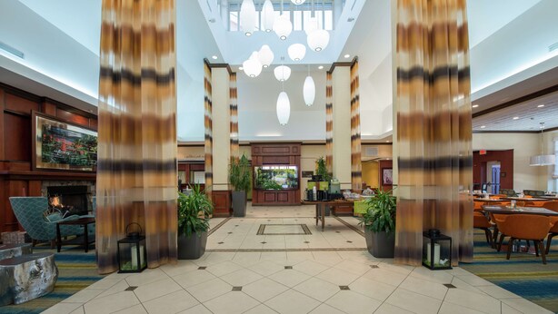 A spacious lobby with a central reception desk, large potted plants, and a modern chandelier. - Hilton Garden Inn Tupelo (Tupelo)
