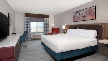 A hotel room with a large bed, a desk, a chair, a TV, and a window with curtains.