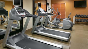 Une salle de sport équipée de tapis de course, de vélos elliptiques et d’un téléviseur fixé au mur.