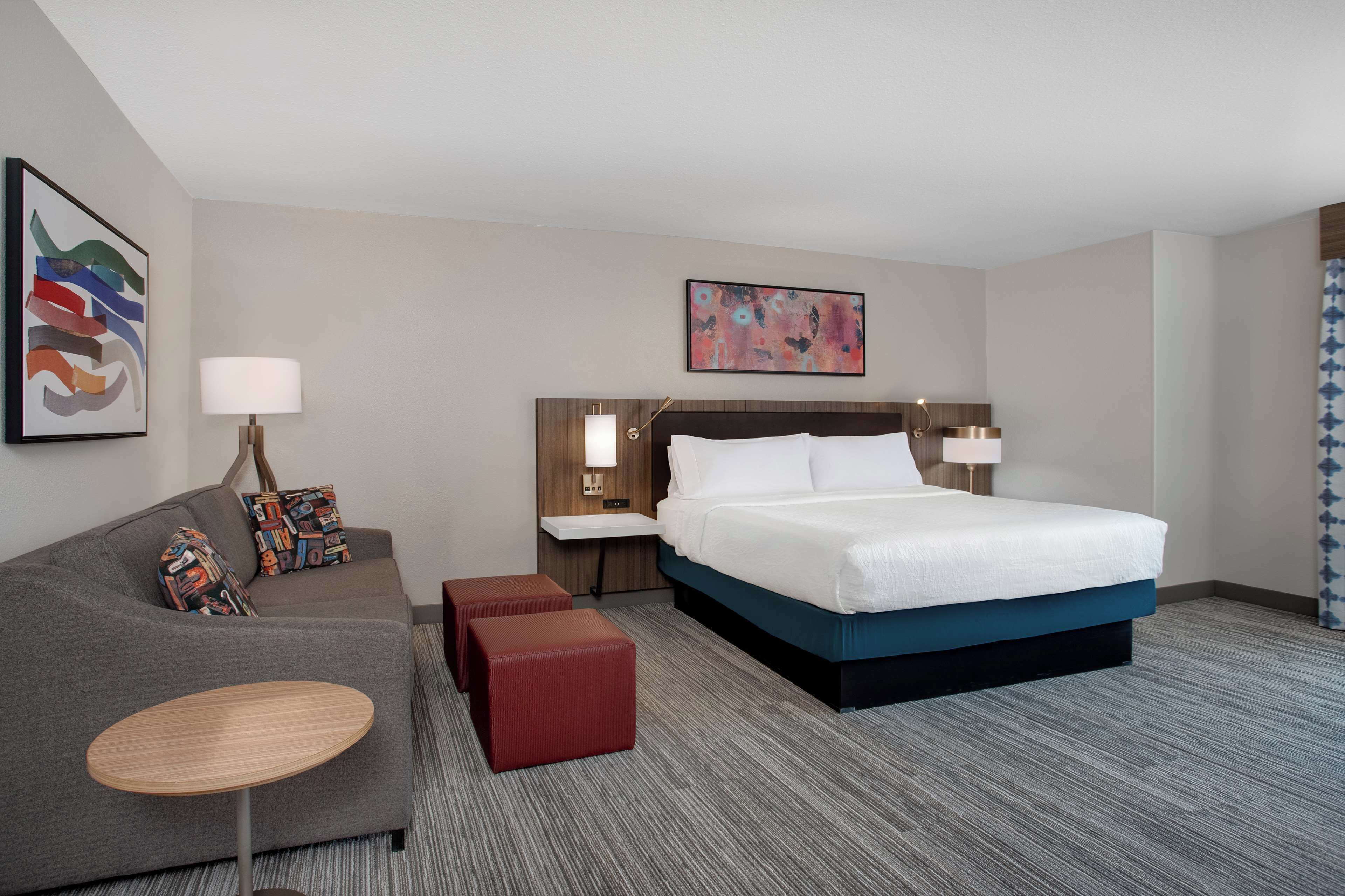 A hotel room with a large bed, a sofa, a small table, and two nightstands with lamps.