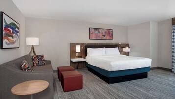 A hotel room with a large bed, a sofa, a small table, and two nightstands with lamps.