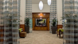A spacious lobby with a high ceiling, multiple hanging pendant lights, and striped curtains.