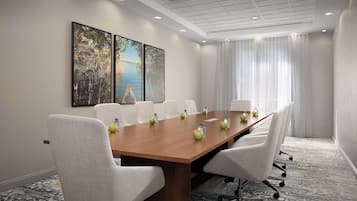 Une salle de conférence avec une longue table, des chaises blanches et des œuvres d’art accrochées aux murs.
