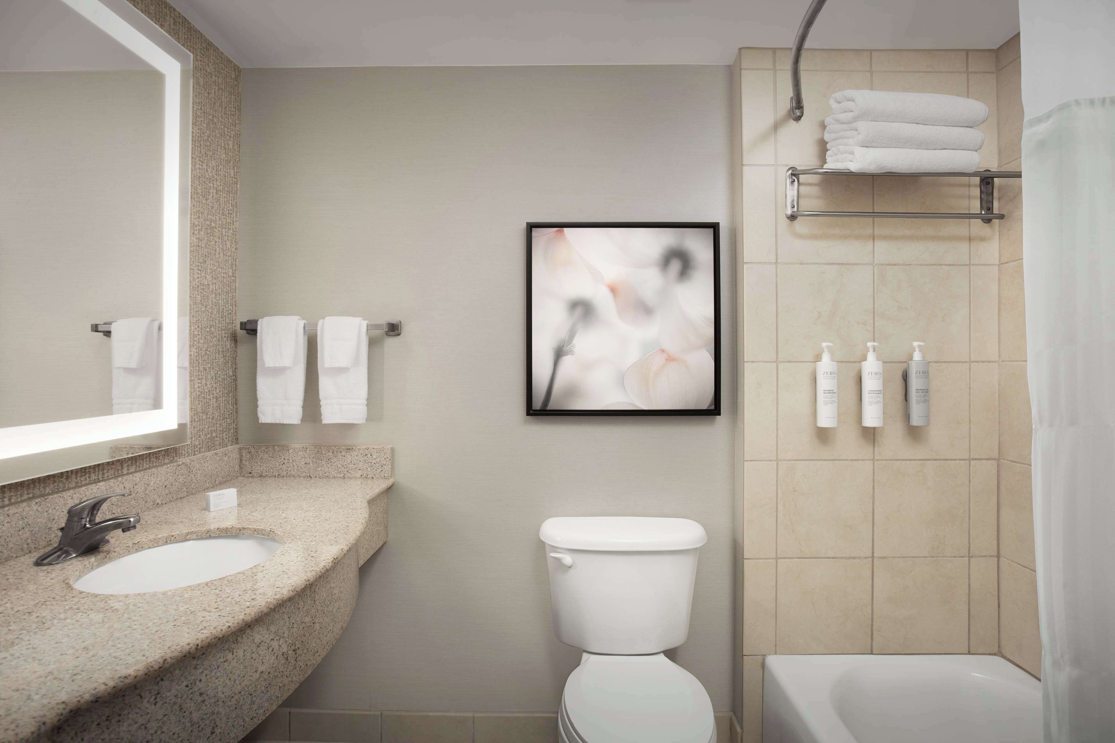Ein Badezimmer mit Waschbecken, Toilette und Badewanne. Handtücher und Toilettenartikel befinden sich an der Wand.