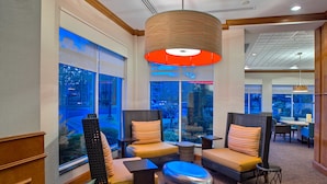 A modern hotel lobby with wicker furniture, large windows, and a central light fixture.