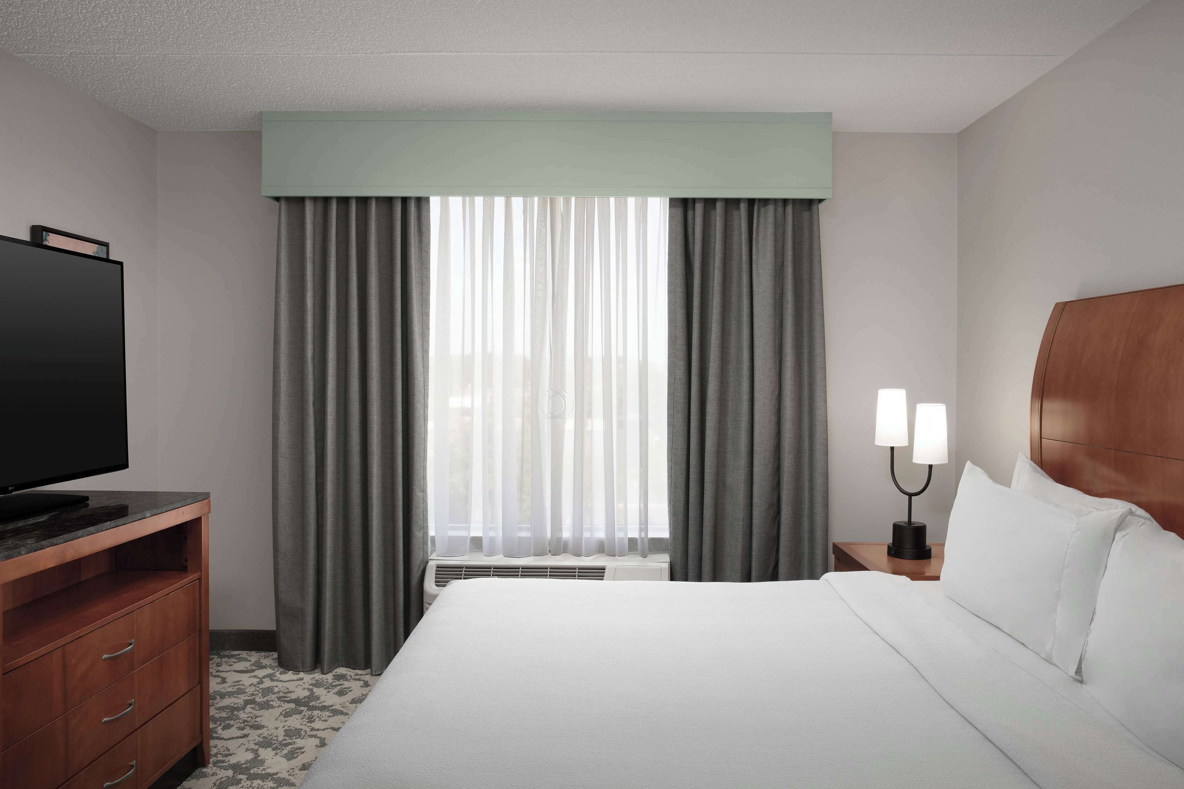 Een hotelkamer met een bed, een televisie, een nachtkastje met lamp en een raam met gordijnen.