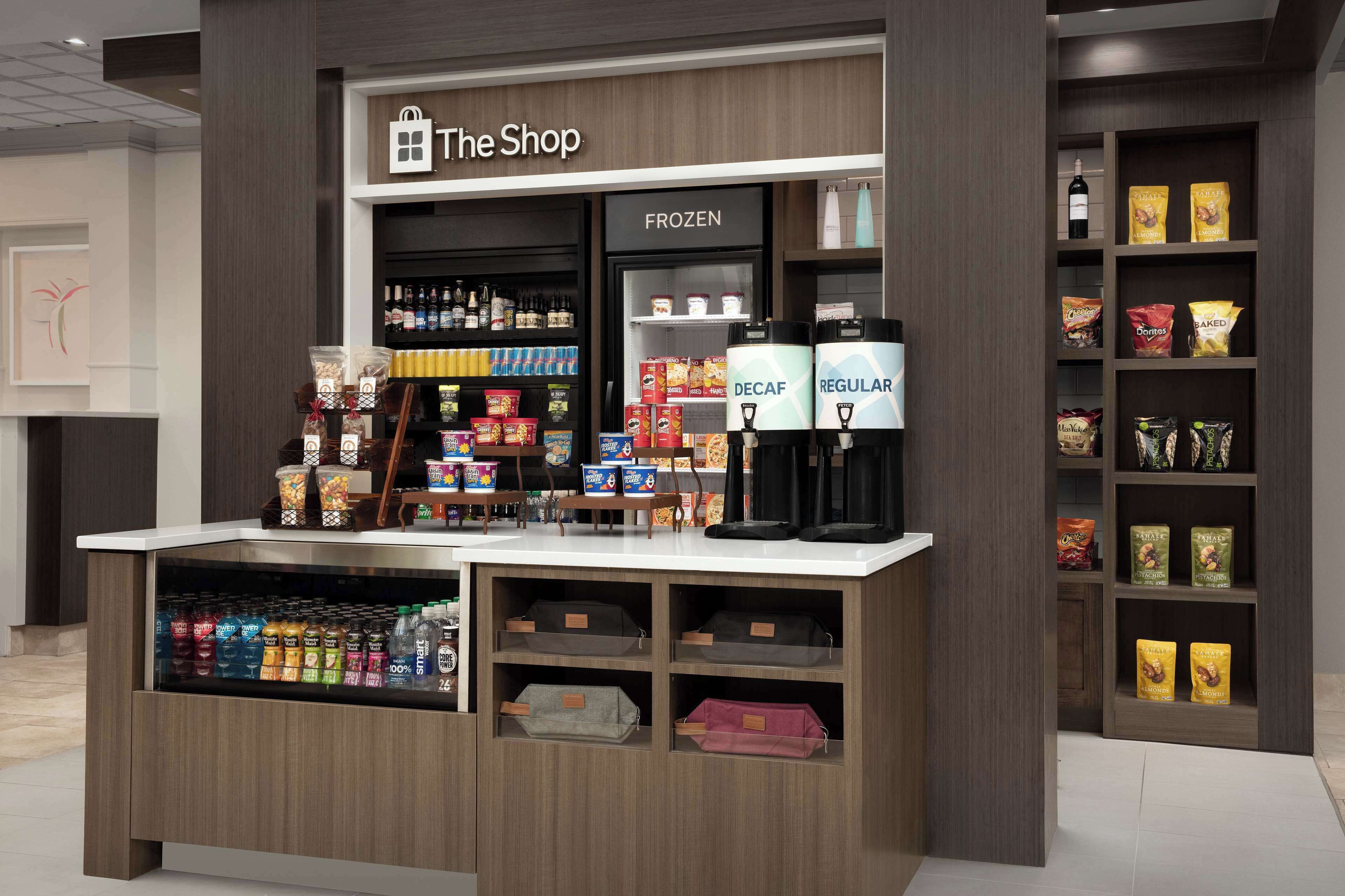 A store named 'The Shop' with shelves of snacks, beverages, and a coffee machine.