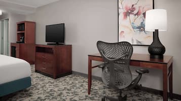 Una camera d'albergo con un letto, una scrivania con una sedia, una televisione, una lampada e una libreria.