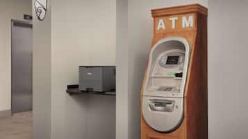 A hotel room with a wooden cabinet labeled "ATM" containing a cash dispenser and a printer.