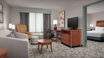 A hotel room with a sofa, armchair, desk, television, and a bed.