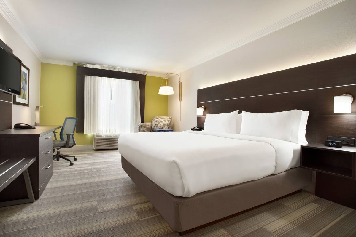 A hotel room with a large bed, a desk with a chair, a TV, and a window with curtains.