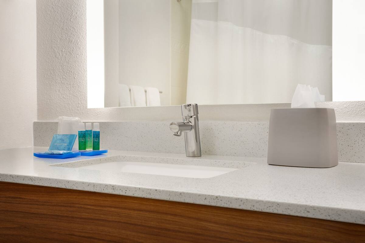 A bathroom with a white sink, a mirror, and toiletries on the counter.