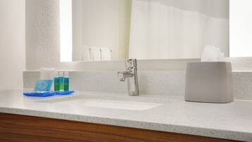 A bathroom with a white sink, a mirror, a faucet, and toiletries on the counter.