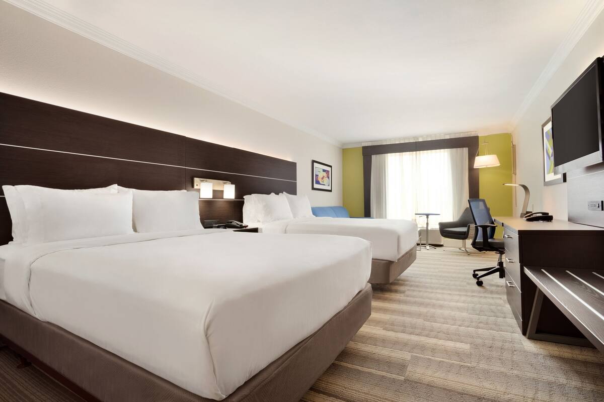 A hotel room with two beds, a desk, a chair, a TV, and a window with curtains.