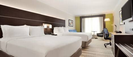 Quarto de hotel com duas camas, uma escrivaninha, uma cadeira, televisão e janela com cortinas.