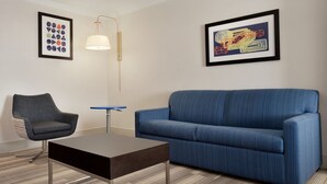 A modern living room with a blue sofa, a dark wooden coffee table, a grey armchair, and a floor lamp. Two framed artworks are hung on the wall. - Holiday Inn Express & Suites Dallas NE - Allen by IHG (Allen)