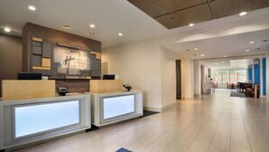 A hotel reception area with a modern design, featuring a reception desk, a digital information kiosk, and a wall-mounted sign.