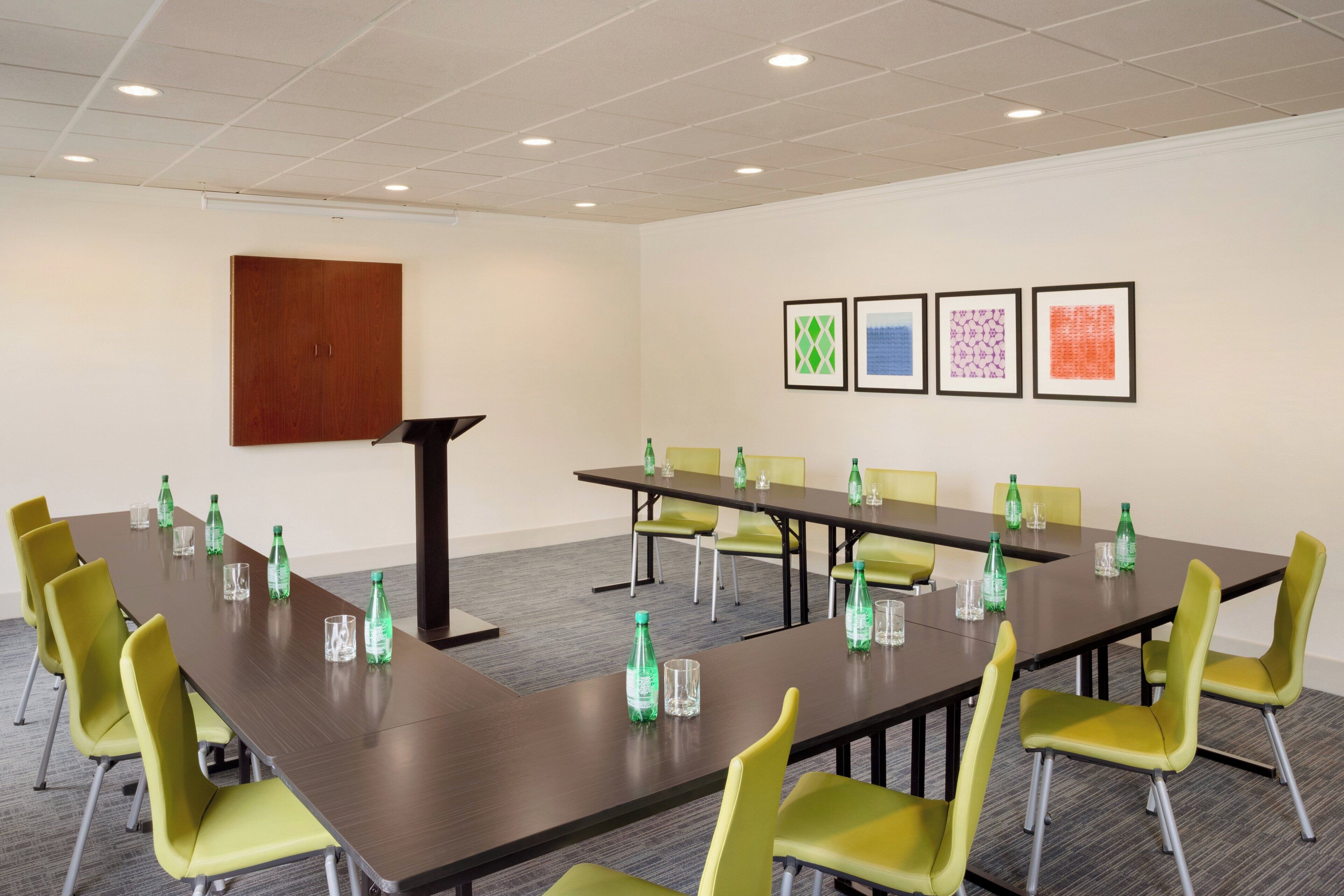 Une salle de conférence avec une longue table, des chaises jaunes et des œuvres d’art encadrées accrochées au mur.