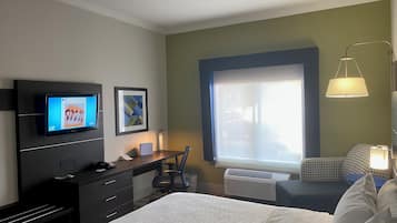 A hotel room with a bed, desk, chair, TV, artwork, window, and lamp.