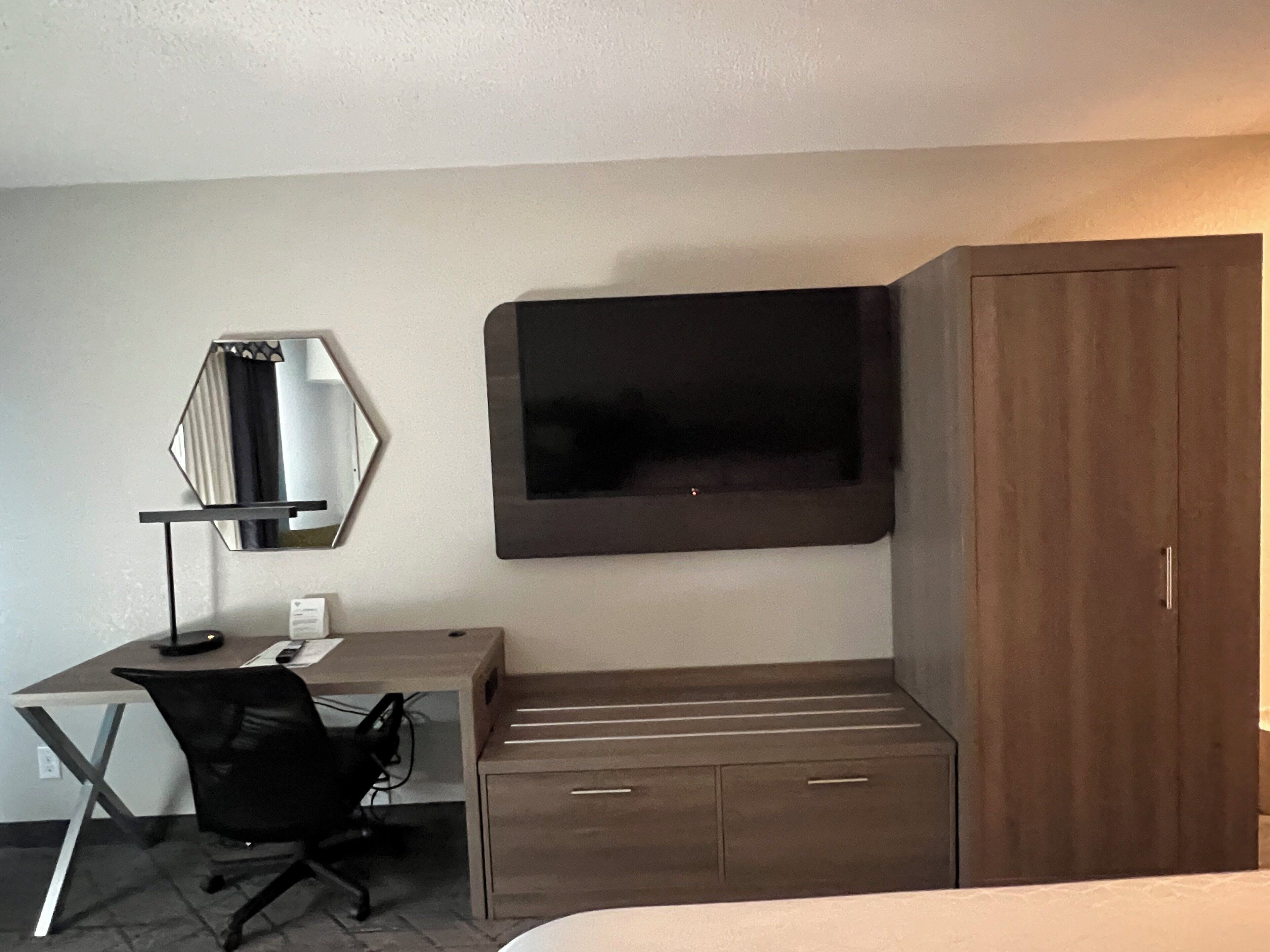 Habitación de hotel con escritorio, silla, televisor, armario y espejo.