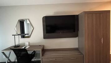 Habitación de hotel con escritorio, silla, televisor, armario y espejo.