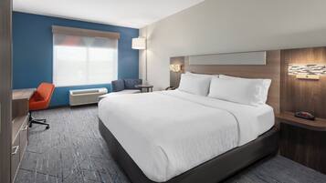 A hotel room with a large bed, a desk with a chair, a small table, and a window with blinds.