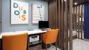 Ein moderner Büroraum mit Schreibtisch, zwei orangefarbenen Stühlen, einem Computer und gerahmten Kunstwerken an der Wand.