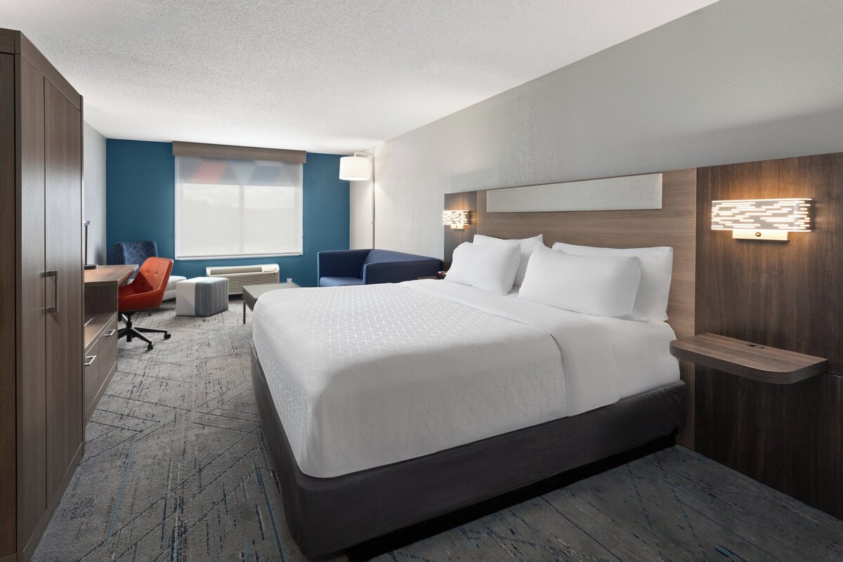 A modern hotel room with a large bed, a desk, a chair, and a small table.