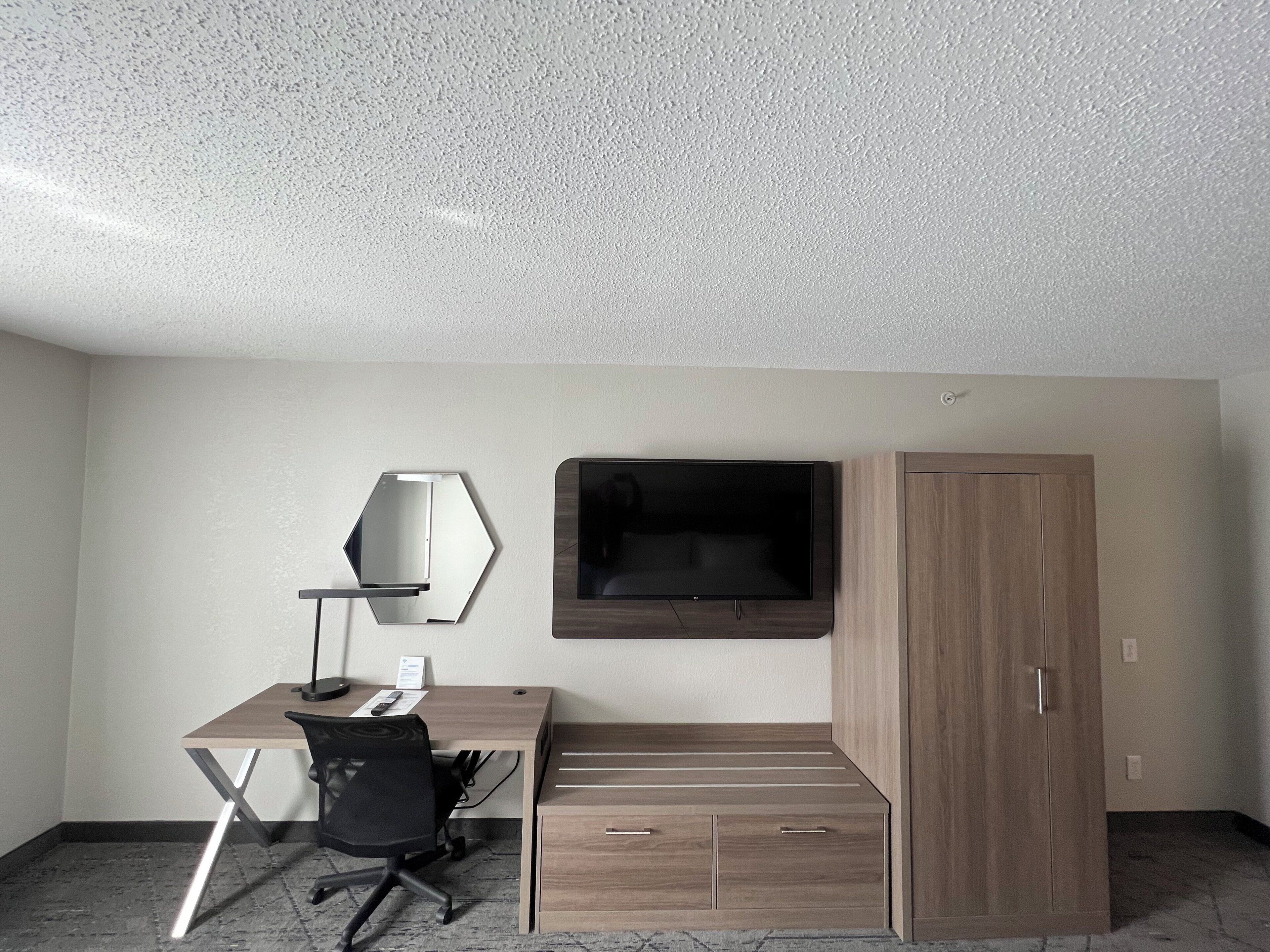 Ein modernes Zimmer mit Schreibtisch, Stuhl, Fernseher und Kleiderschrank.