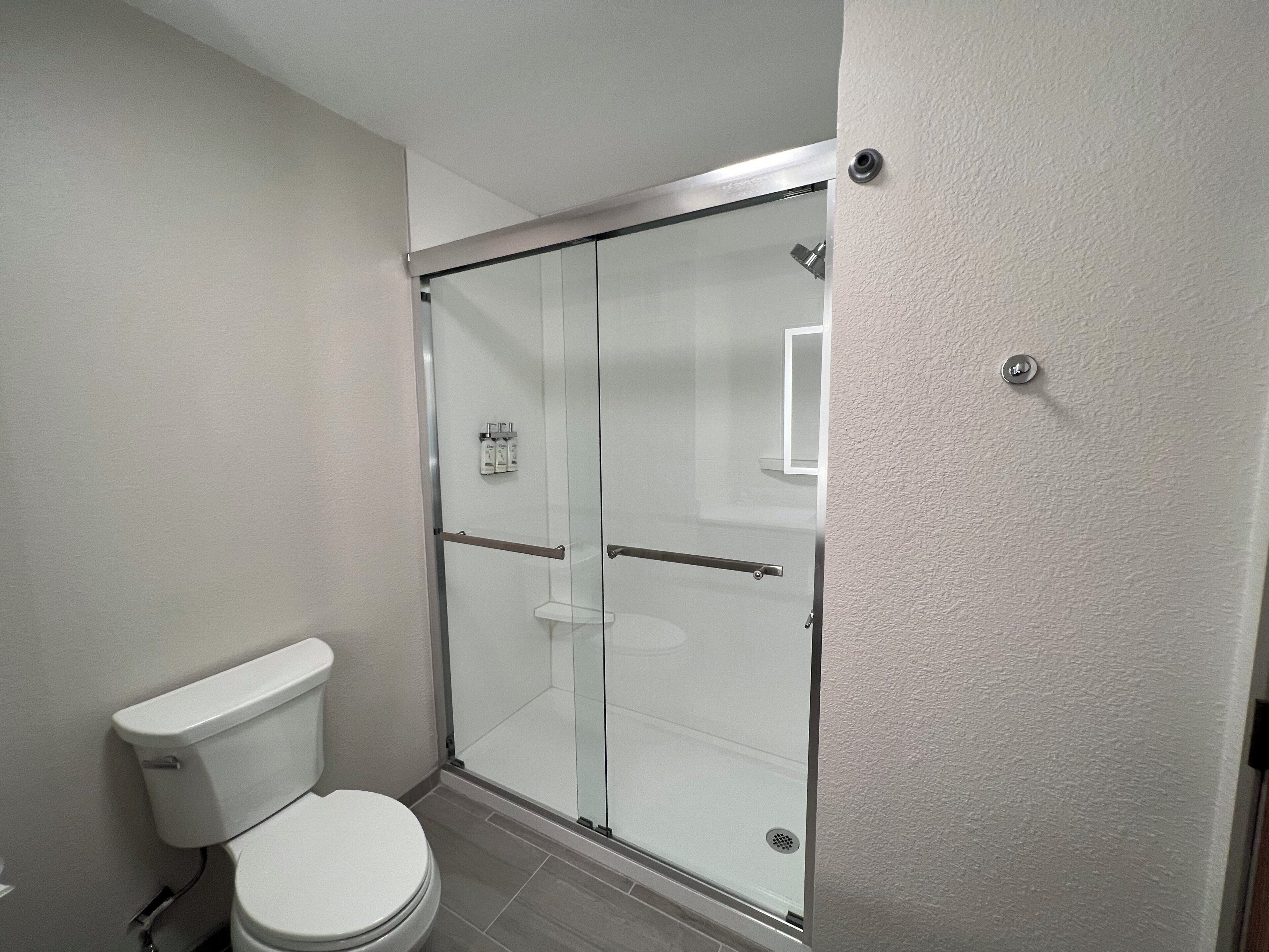Un baño con inodoro, ducha con mampara de vidrio y pared blanca.