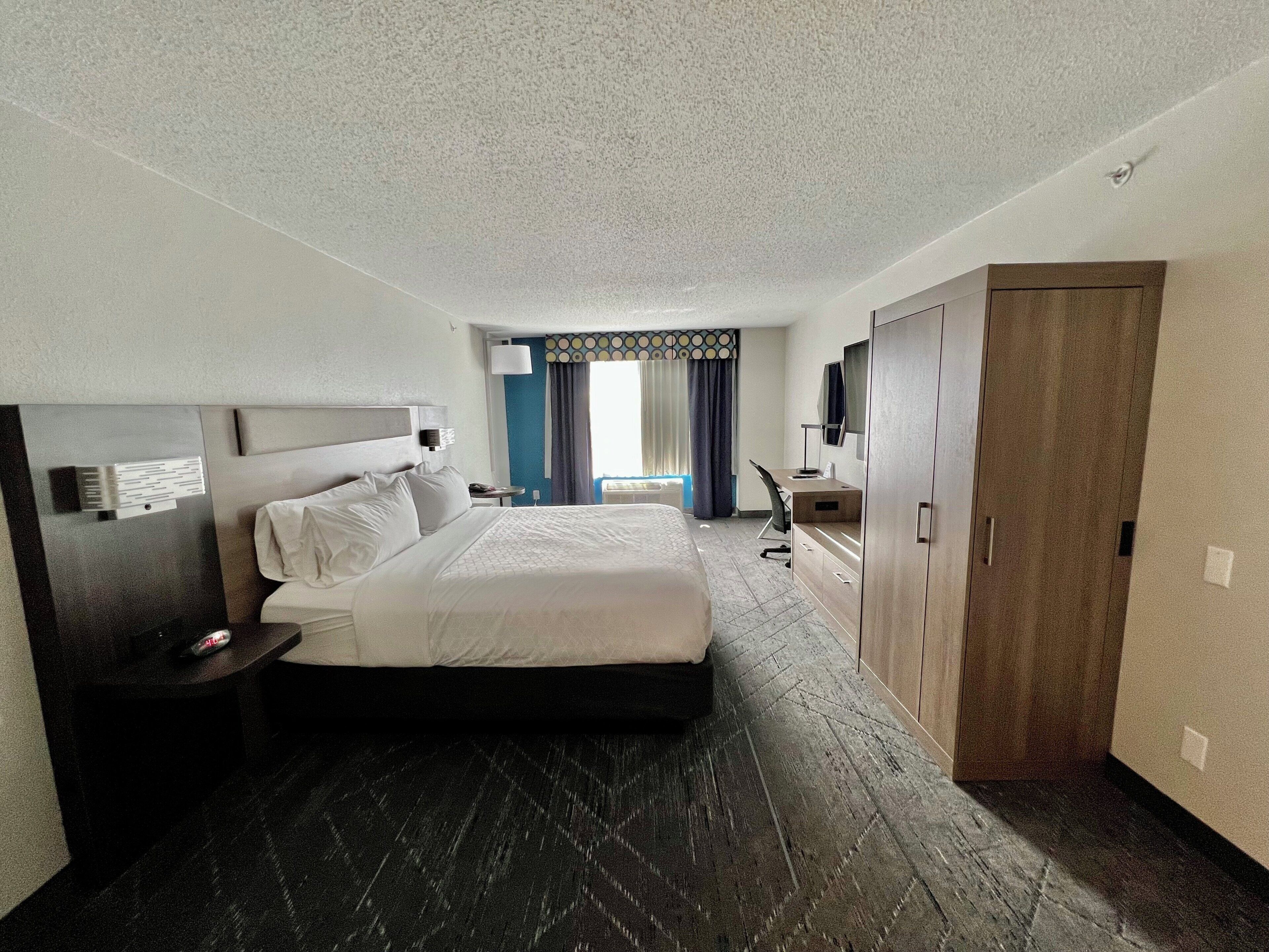 A hotel room with a large bed, a desk, a wardrobe, and a view of the outdoors.