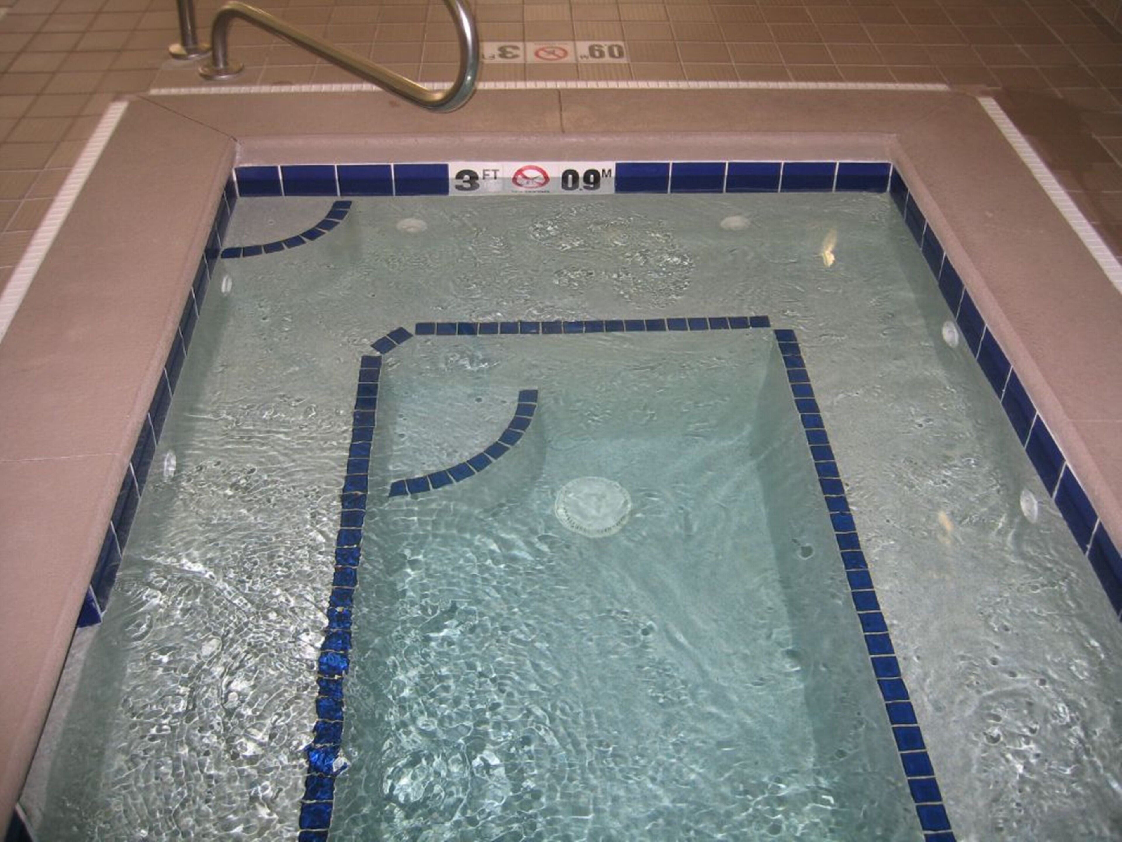 A rectangular pool with blue tiles and a handrail, surrounded by a tiled floor.