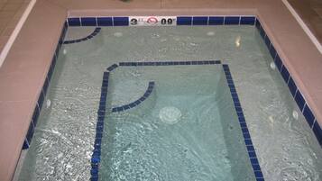 A rectangular pool with blue tiles and a handrail, surrounded by a tiled floor.