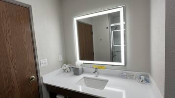 Une salle de bain avec un lavabo blanc, un miroir avec un éclairage intégré, un porte-serviettes et une porte en bois.