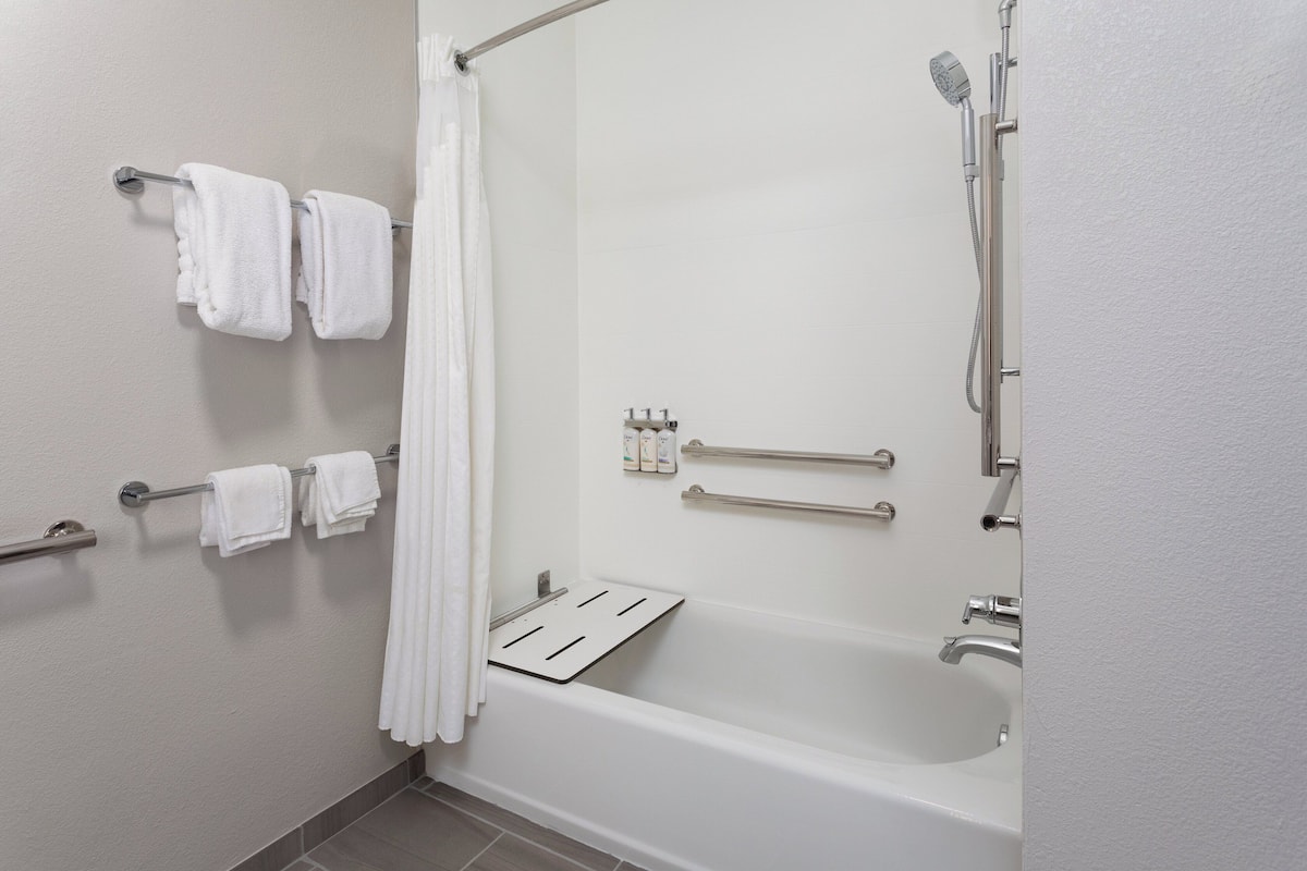 Une salle de bain moderne équipée d’une baignoire, d’une douche et de barres d’appui.