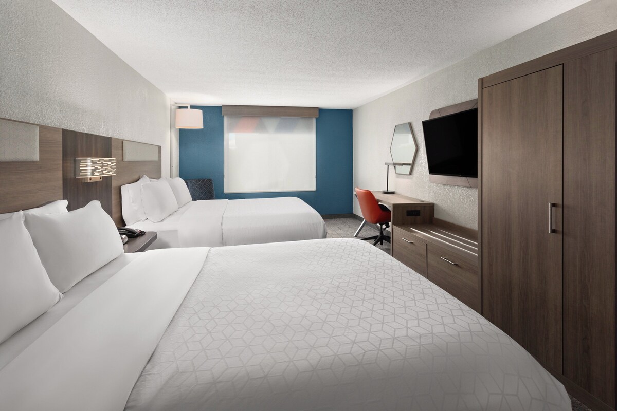 A hotel room with two beds, a desk, a TV, and a window with a view.