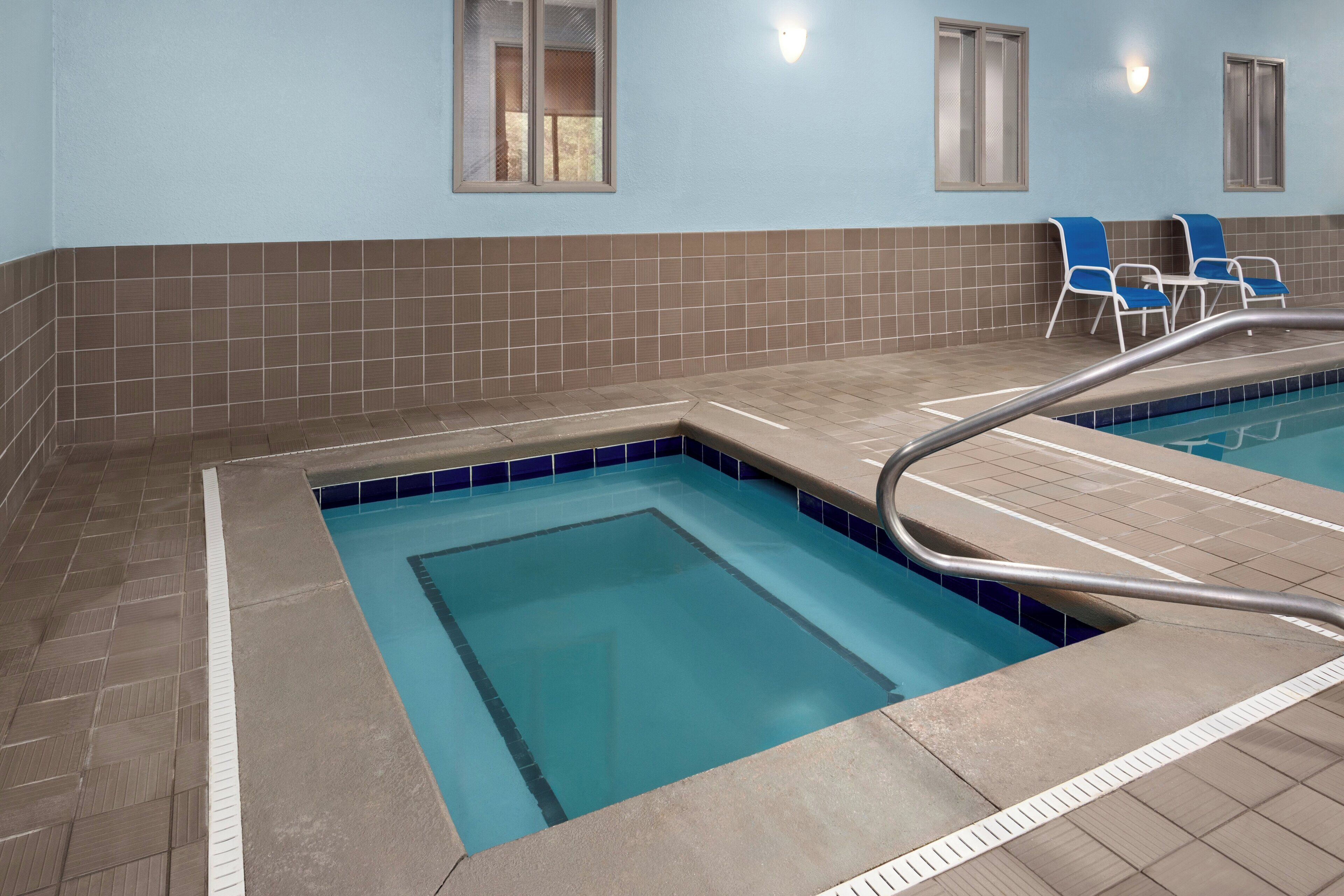 An indoor swimming pool with a tiled edge, a metal pool ladder, and two blue lounge chairs.