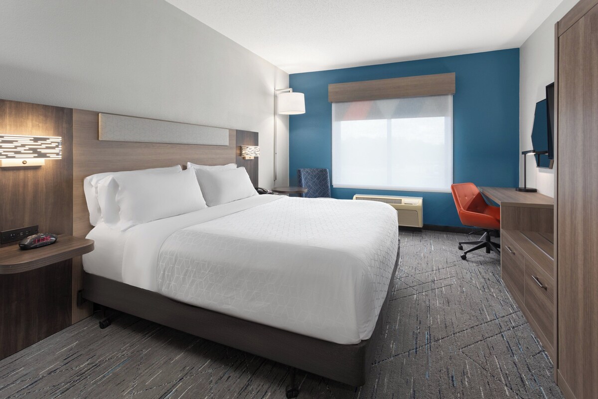A modern hotel room with a large bed, a desk, a chair, and a TV on the wall.
