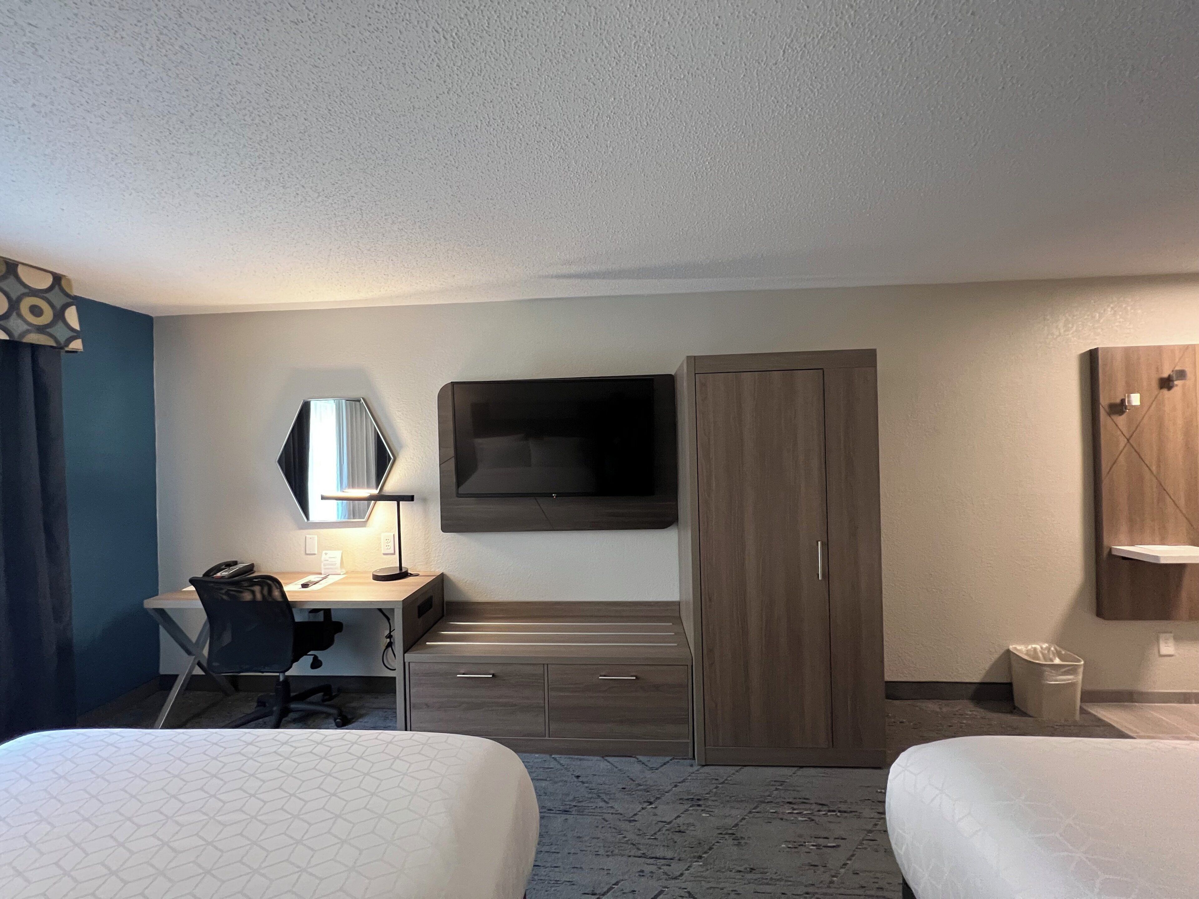 A hotel room with two beds, a desk with a chair, a television mounted on the wall, and a wardrobe.